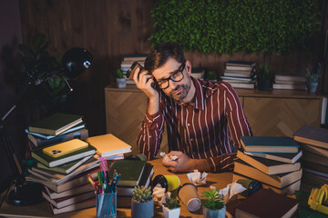Naklejka premium Young man studying late at night in a cozy home environment while surrounded by books and educational materials