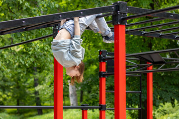 Young girl hanging upside down on bright outdoor fitness equipment