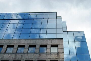 A modern building features a facade of reflective glass panels, capturing the sky and clouds above. The geometric lines and symmetry create a sleek and contemporary architectural design.