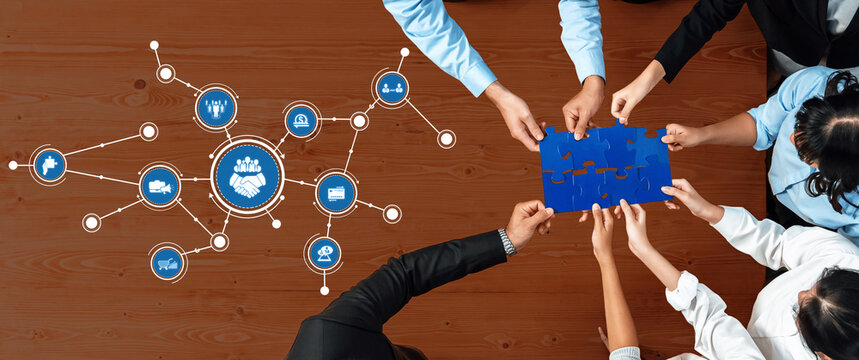 A group of professionals collaborates at a meeting, placing a blue puzzle piece on a wooden table. The digital icons symbolize connection and strategic partnerships. Amity