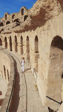 Stylish tourist wearing a hat explores the historic Colosseum in El Jem, Tunisia, vertical video