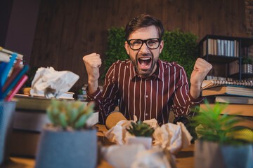 Young man enthusiastically reacting with clenched fists in a casual setting, surrounded by books...