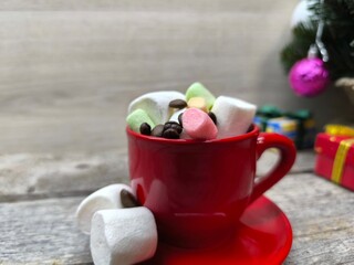 a red cup filled with marshmallow slices. There is a Christmas tree in the background