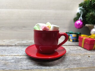 a red cup filled with marshmallow slices. There is a Christmas tree in the background