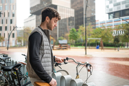 Young man picking up his bicycle from urban bicycle parking