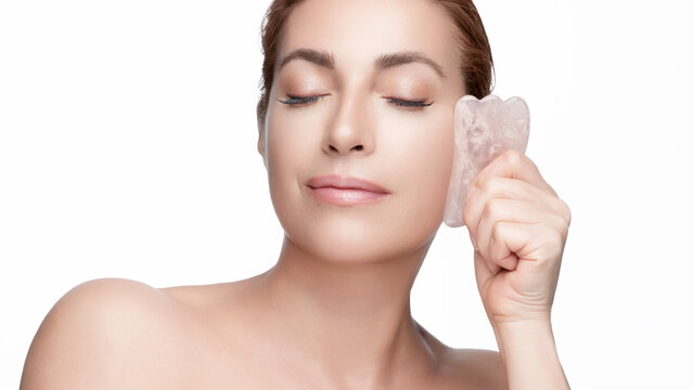 Woman practicing facial massage with a gua sha rose quartz tool