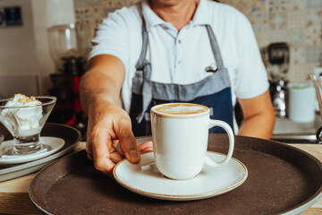photo of unrecognizable senior latin colombian barista delivering a cappuccino with late art on tray in coffee shop