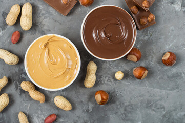 Peanut butter and chocolate spread on toast and in bowl, peanuts and hazelnuts on dark grey...