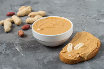Peanut butter spread on toast and in bowl, peanuts on dark grey background. Horizontal