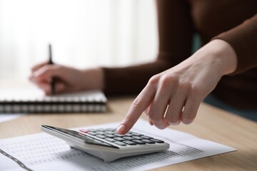 Budget. Woman with paperwork and calculator at wooden desk indoors, closeup