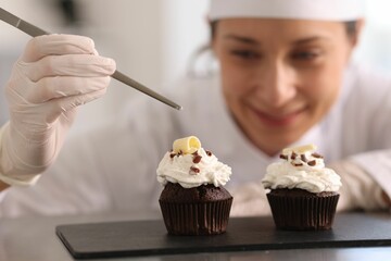 Confectioner with tweezers decorating cupcake at table, selective focus