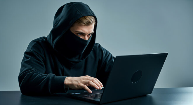 Caucasian young male in hooded attire using laptop for cyber activity