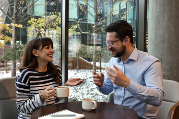 Happy colleagues talking during coffee break at wooden table in cafe