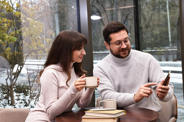 Colleagues with smartphone having coffee break at wooden table in cafe