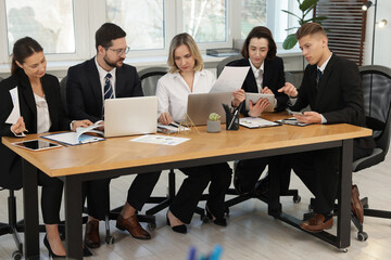 Coworkers with different devices working together at wooden table in office