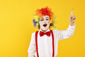 Emotional little boy dressed like clown pointing upwards on yellow background, space for text....