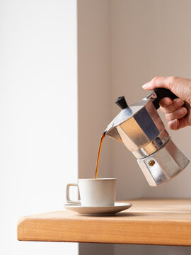 Person pouring coffee from moka pot into cup on wooden table