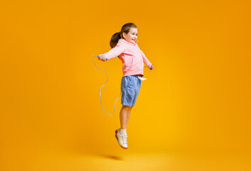 Cute little girl with jump rope on yellow background