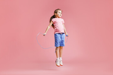 Cute little girl with jump rope on light pink background © New Africa