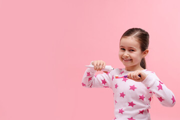 Cute girl applying toothpaste onto toothbrush on pink background, space for text