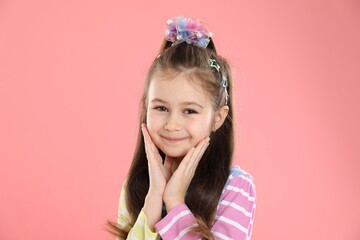 Happy little girl wearing beautiful hair accessories on pink background
