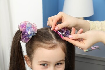 Mom putting cute accessories onto her daughter's hair at home, closeup