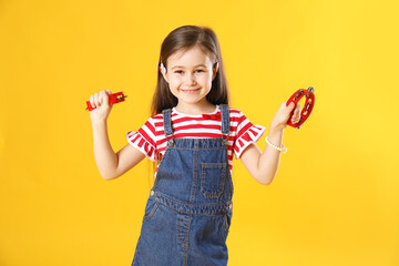 Cute girl playing toy tambourines on yellow background
