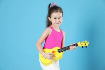Cute girl playing toy guitar on light blue background