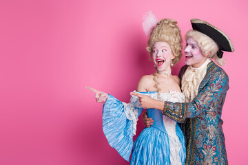 Cheerful couple in antique costumes celebrate at a vibrant party with laughter and joy on a pink...