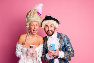 Elegant young couple in period costumes enjoying modern technology against a pink background