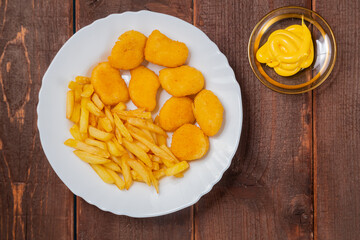 French fries and golden nuggets with cheese sauce on a wooden table