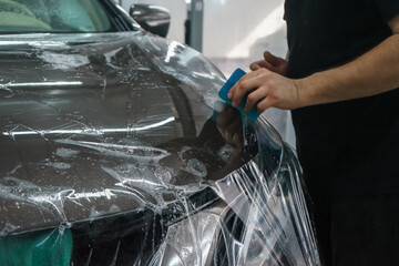 Worker smoothing transparent protective film on car hood. Car wrapping with protective film.