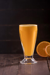 Fresh Orange Juice served in a tall glass with sliced oranges on a dark background and a wooden table side view of refreshing and healthy citrus beverage
