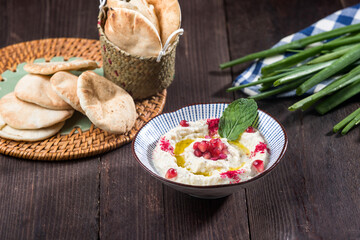 Mutabal, a creamy eggplant dip served in a bowl with pita bread on a wooden table topped with...