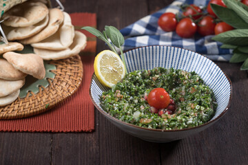 Tabbouleh Salad with parsley, lemon, tomatoes, and pita bread served in bowl isolated wooden table side view of healthy Middle Eastern salad