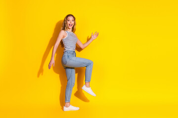 Young woman playfully posing against vibrant yellow background showcasing casual fashion in denim...