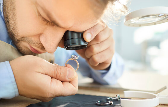 Jewellery inspector doing visual examination of jewelry ring, experienced male jeweler detects damages, quality, price for jewelry trader and gem expert with magnifying glass or jeweler's loupe 