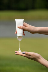 White cosmetic tube held in a hand against a blurred green outdoor background