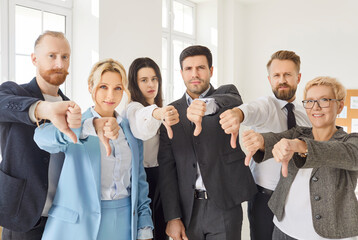 Portrait of business people standing in a row in office and showing thumbs down sign looking at...