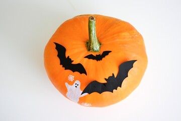 Halloween pumpkin head on table with bat decor and ghost painted on pumpkin.