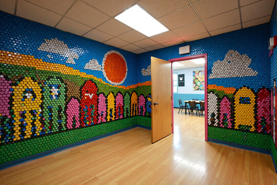 classroom wall entirely covered in a colorful mosaic created from buttons, depicting a whimsical landscape with houses, clouds, and a bright sun, creating an immersive and stimulating learning environ