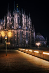 Fototapeta premium In the stillness of late evening, Cologne Cathedral comes alive in a unique way, bathed in the warm light of the street lamps illuminating its surroundings. This photo captures the majestic cathedral 