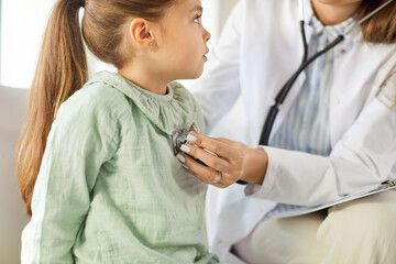 Cropped shot of female pediatrician using stethoscope, checking heartbeat of little girl patient...