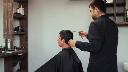 A skilled hairdresser expertly cuts hair on a client at a stylish barbershop, showcasing a clean and modern environment. The atmosphere is lively, with tools at hand