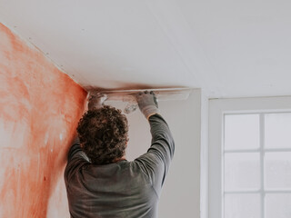 A Caucasian young man is putting putty on the wall.