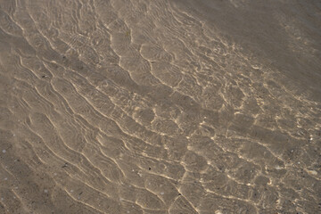 A mesmerizing view of sunlight reflecting on shallow water, creating rippling patterns on the sandy ocean floor.
