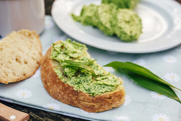 Slice of bread with wild garlic butter on floral cloth in spring forest