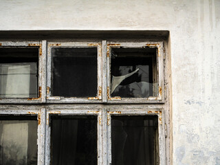 Old, weathered window with peeling paint and a broken glass pane in a deteriorated building facade. The image captures a sense of neglect, decay, and the passage of time