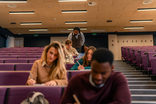 University students taking exam with professor watching over in lecture hall