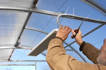 Protecting vegetable crops from spring cold in a greenhouse. A man leads an electric cable laid in...